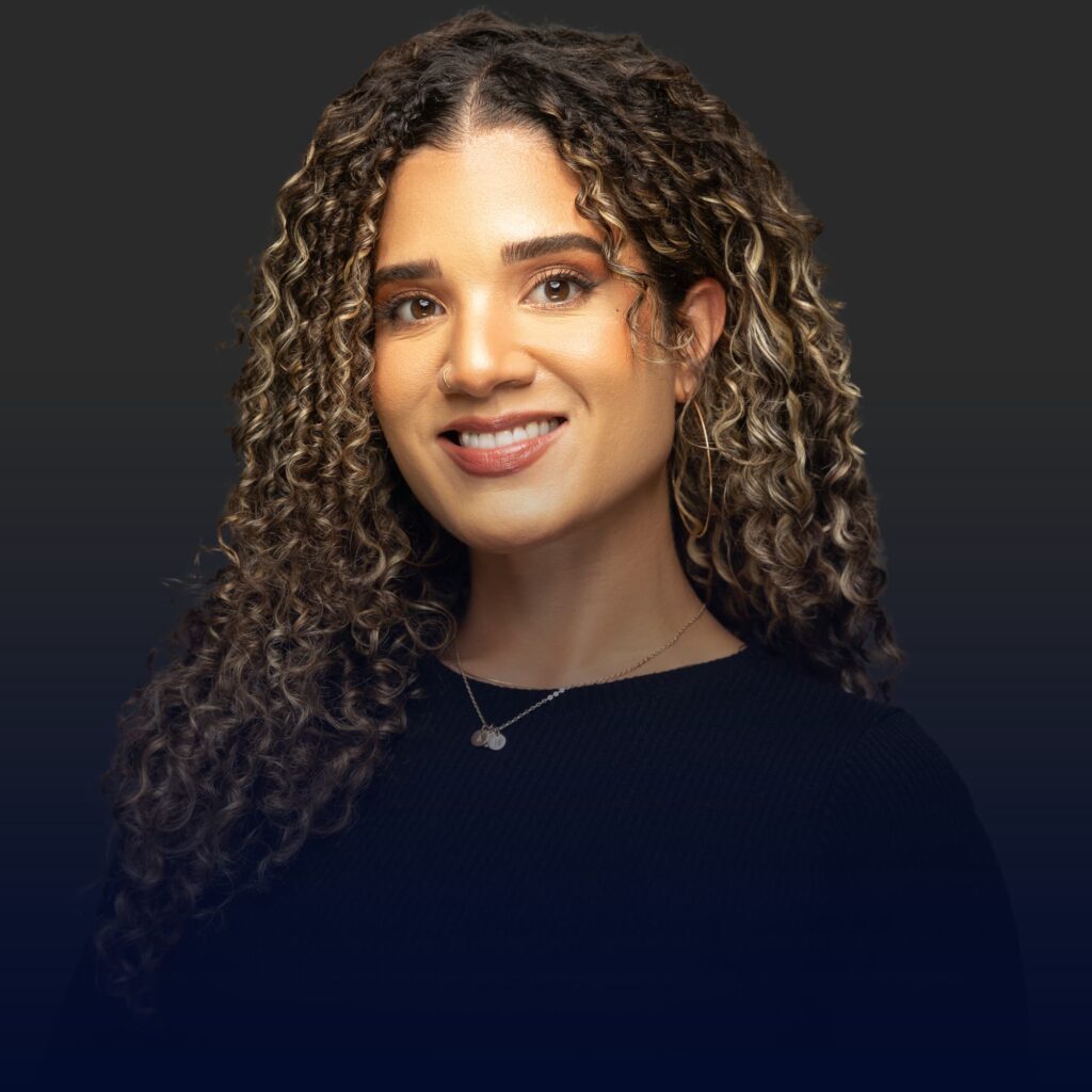 A smiling woman with curly brown hair wearing a black top and necklace