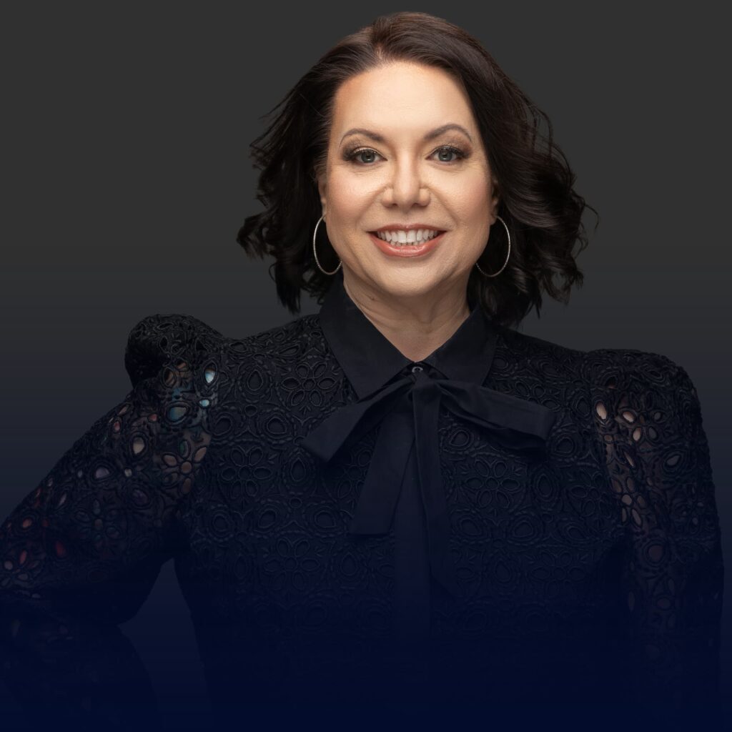 Portrait of a smiling woman with long dark hair, wearing a black lace-trimmed blouse and hoop earrings, against a dark background.