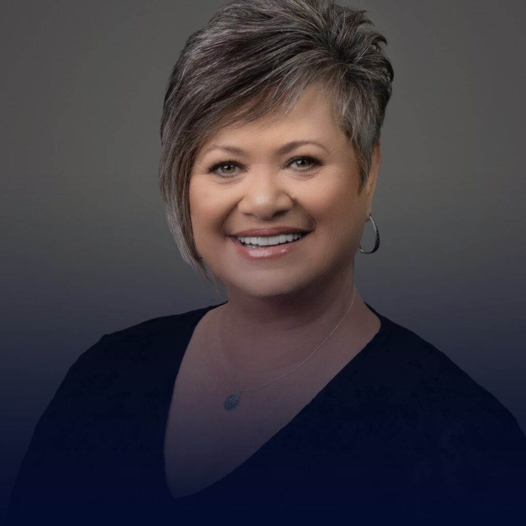 A smiling woman with short gray hair wearing a black top and earrings